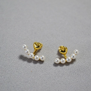 Close-up of golden heart earrings with curved white pearl drop on grey background