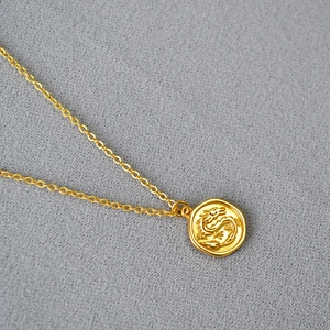 Detailansicht der goldenen Halskette mit Drachenrelief und feiner O-Kette in Mattgold