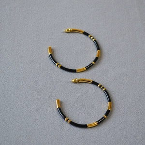 Detail showing oversized black enamel C-shaped hoop earrings with gold bamboo sections