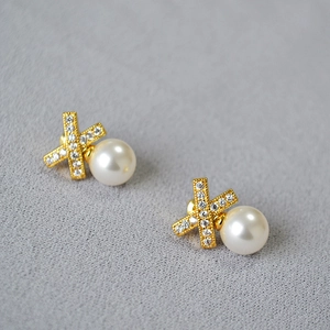 Macro shot of French style X-cross gold earrings with shimmering cubic zirconia and pearls