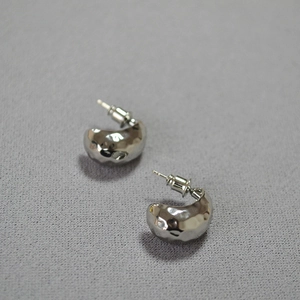 Macro detail of silver C-shape earrings with a textured hammered finish on a fabric background