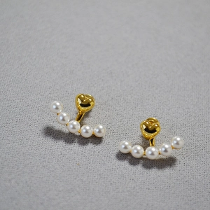 Elegant gold heart earrings with white pearl hangings on a textured background