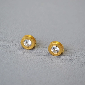 Macro detail of gold-plated stud earrings with brushed texture and central zircon stone