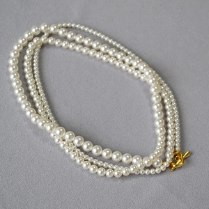 Detail of multi-layer pearl necklace with golden OT clasp on grey textured fabric