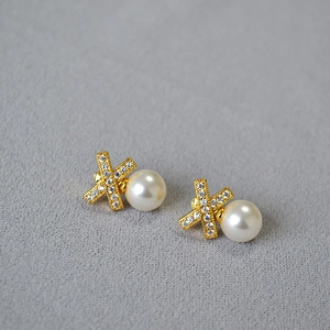 Macro shot of X-shaped gold stud earrings with white pearls and sparkling zircon inlays