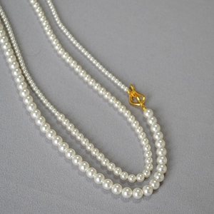Detail of layered pearl necklace featuring gold OT toggle clasp on grey textured fabric