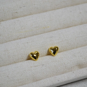 Macro shot of polished gold heart-shaped stud earrings on a textured cream display tray