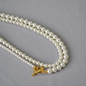 Detail of double-layer pearl necklace with golden OT clasp on grey textured fabric
