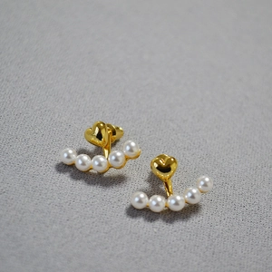 Detail view of gold heart stud earrings with curved white pearl arrangement