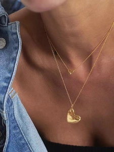 Détail de colliers superposés cœur doré avec texture martelée sur modèle en jean