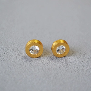 Detailed view of gold round studs with brushed texture and sparkling zircon center