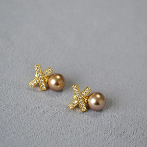Detailed shot of X-shaped gold earrings with zircon stones and champagne pearls