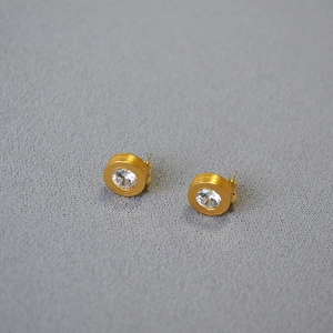 Detail of round gold-plated stud earrings with brushed texture and sparkling zircon