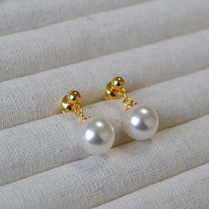 Elegant gold pearl drop earrings featuring round white pearls on a cream jewelry tray