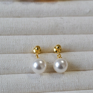 Close-up of elegant round white pearl earrings with gold-tone studs on a fabric tray