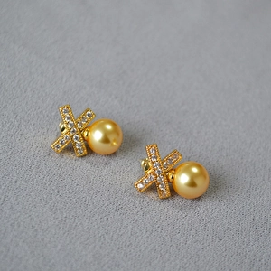 Detailed macro view of X-shaped gold-plated stud earrings with pearls and pavé cubic zirconia