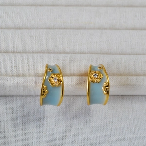 Close-up of golden C-shaped hoop earrings with blue enamel and daisy zircon details