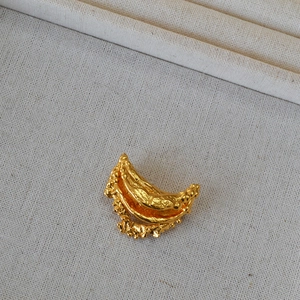 Detailed macro view of irregular gold-plated lava texture crescent brooch on linen fabric