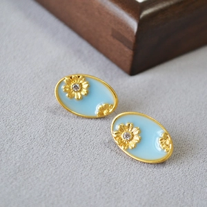 Detailed view of oval enamel earrings with gold daisies and sparkling zircon stones