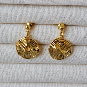 Macro detail of gold plated disc earrings with concentric tree ring texture and glossy finish