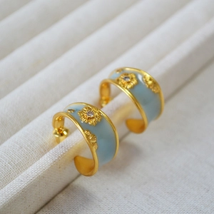 Macro shot of French style C-shape earrings with light blue enamel and golden sunflowers