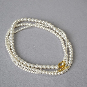 Detail of cream white triple-strand pearl necklace with golden OT clasp on grey fabric