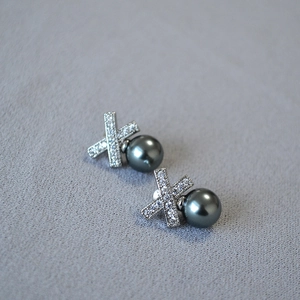 Close-up of X-shaped silver earrings with sparkling cubic zirconia and dark grey pearls