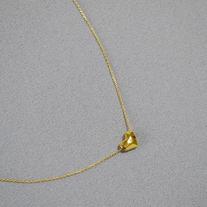 Collier avec pendentif cœur martelé en or poli et chaîne fine sur fond de tissu neutre