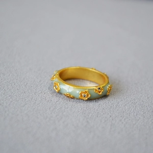 Detailed close-up of gold-plated brass ring with green enamel flowers and white zircons