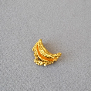 Irregular lava texture moon-shaped gold brooch on a minimalist fabric background