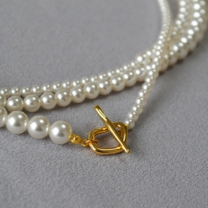 Elegant multi-layered pearl necklace with golden OT buckle clasp on grey fabric background