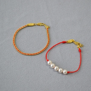 Detail of red braided pearl bracelet and gold bead cord bracelet with metal logo charm