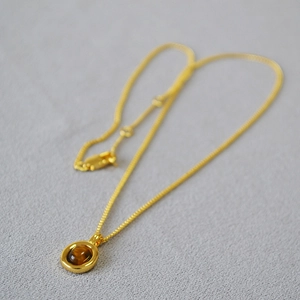 Retro tiger eye stone necklace in gold-plated brass with round pendant on grey fabric