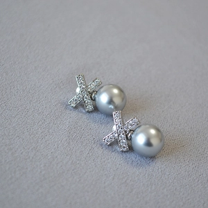 Close-up of X-shaped zircon-encrusted silver earrings featuring elegant grey pearls