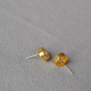 Detailed close-up of golden cylindrical earrings with sparkling cubic zirconia inlay