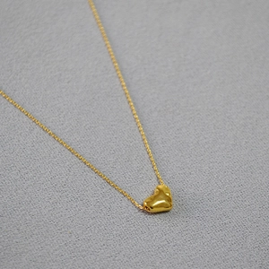 Gros plan d'un pendentif cœur doré avec une texture martelée sur une fine chaîne dorée