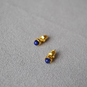 Minimalistische vergoldete Ohrstecker mit blauem Lapislazuli auf grauem Stoff