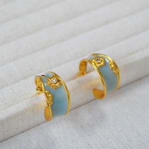 Detail of gold C-hoop earrings with light blue enamel and sunflower zircon accents