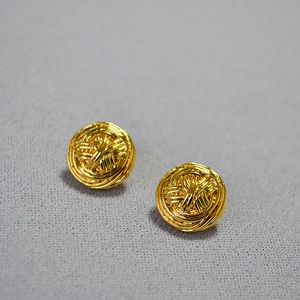 Detailed view of golden woven textured round stud earrings on a dark grey fabric