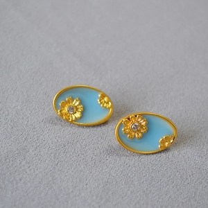 Close-up of gold-plated oval stud earrings with light blue enamel and daisy motifs