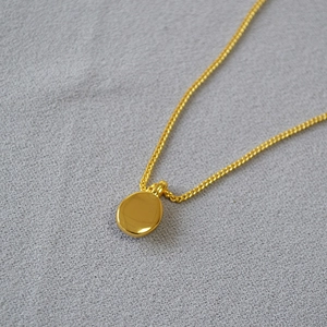 Detail of a minimalist gold oval pendant necklace on a textured grey fabric background