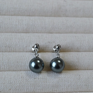 Close-up of elegant black pearl drop earrings with polished silver metal on beige linen