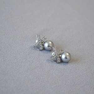 Macro shot of X-shaped zircon stud earrings with elegant grey pearls and silver pins