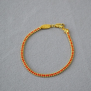 Detail view of woven red string bracelet with gold beads, lobster clasp and oval X charm