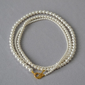 Detailed view of triple-layered pearl necklace with golden OT toggle clasp on grey background