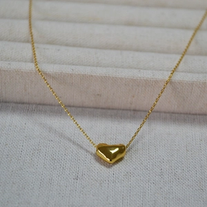Détail d'un pendentif cœur doré minimaliste avec finition miroir sur fond de crème texturé