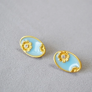 Close-up of oval gold earrings with blue enamel and daisy floral zircon details