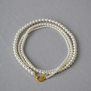 Elegant white pearl necklace with gold OT clasp on a textured gray background
