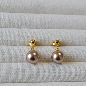 Macro shot of elegant champagne pearl stud earrings with gold pins in a textured jewelry box