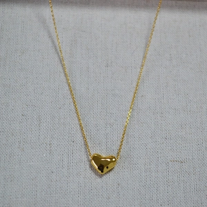 Gros plan du pendentif cœur poli plaqué or 18 carats avec chaîne fine sur tissu gris